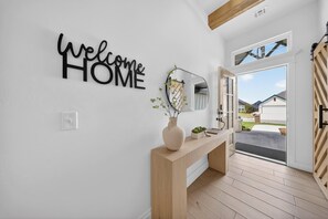 A modern interior with a 'Welcome Home' sign, a mirror, a wooden console table, and a door leading outside. - The Soft Modern House - Designer Home + Cozy Vibes (Oklahoma City)
