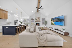 A modern kitchen with white cabinets, a central island, and a dining area with bar stools. - The Soft Modern House - Designer Home + Cozy Vibes (Oklahoma City)