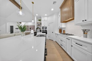 A modern kitchen with white cabinetry, a marble island, and a wooden ceiling beam. - The Soft Modern House - Designer Home + Cozy Vibes (Oklahoma City)