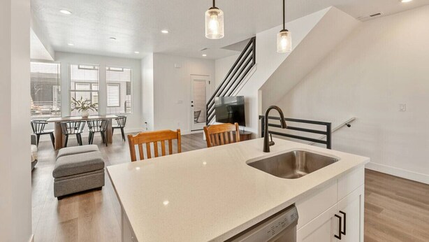 A modern kitchen with a central island, pendant lighting, and a staircase leading to another level. - Foothill Flat | Brand New | Garage | Near Ski Canyons (Sandy)