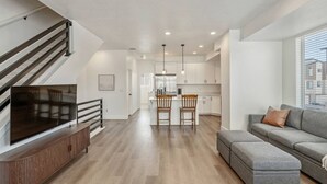 A modern apartment with a living room, kitchen, dining area, and a staircase. - Foothill Flat | Brand New | Garage | Near Ski Canyons (Sandy)