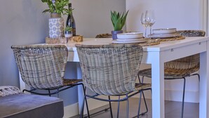 Un comedor con sillas de mimbre, una mesa blanca y una planta en maceta.