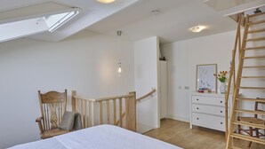 Un dormitorio con cama, silla de madera, cómoda y escalera de madera.