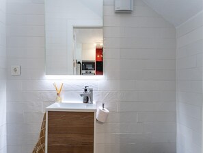 Et badeværelse med en hvid flisevæg, et træbord, et spejl, en hane og en toiletpapirholder.