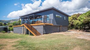 A modern two-story house with a covered outdoor area, a staircase, and a view of the surrounding landscape. - Piwakawaka Haven - Pohara Beach (Pōhara)