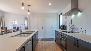A modern kitchen with a central island, built-in appliances, and pendant lighting. - Piwakawaka Haven - Pohara Beach (Pōhara)