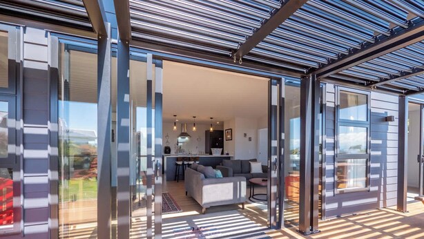 A modern interior with a glass door leading to a living area, a kitchen, and a balcony with a view. - Piwakawaka Haven - Pohara Beach (Pōhara)