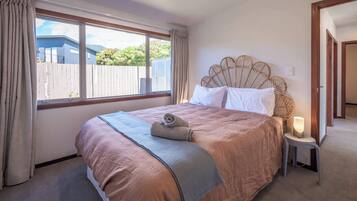 Un dormitorio con una cama grande, una ventana con cortinas, una lámpara de noche y vistas al exterior.