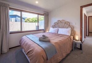 A bedroom with a large bed, a window with curtains, a bedside lamp, and a view of the outside.
