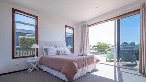 A bedroom with a large bed, a nightstand, a lamp, and a view of the outdoors through a sliding glass door. - Pohara's Beachside Bliss (Pōhara)