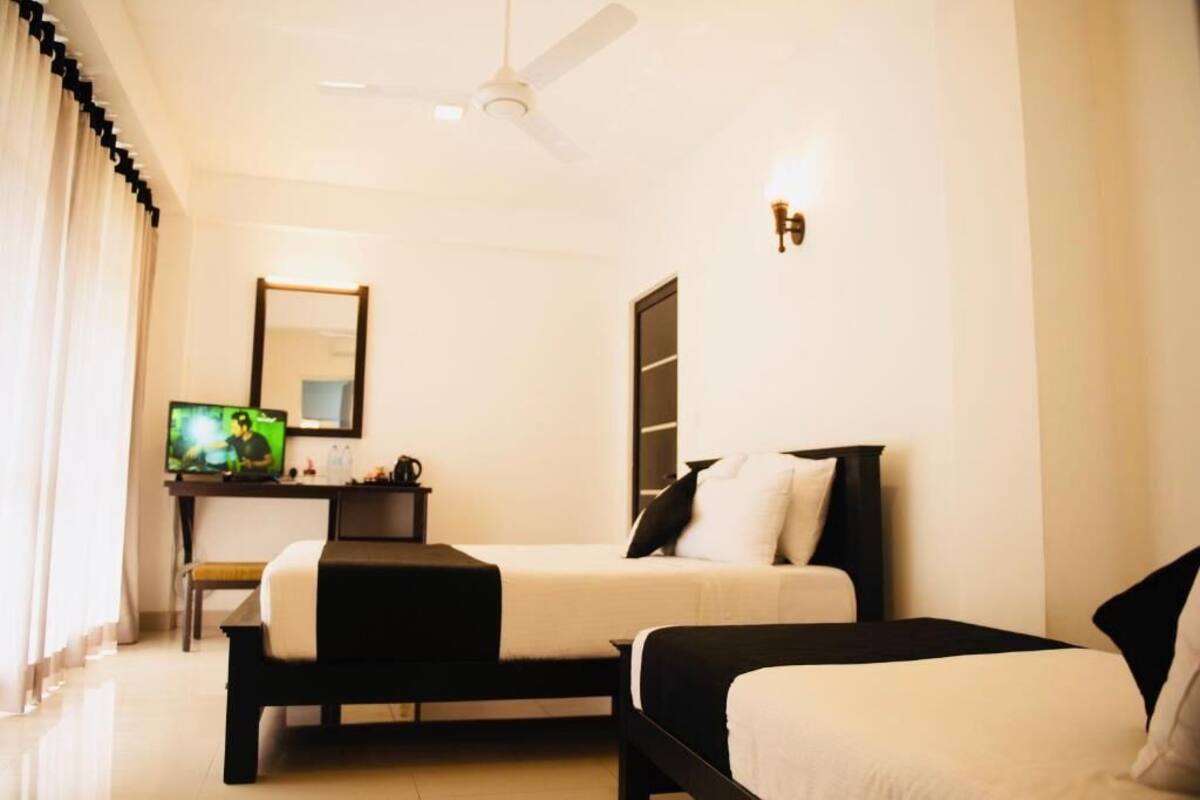 A hotel room with two beds, a desk with a computer, a television, and a ceiling fan.