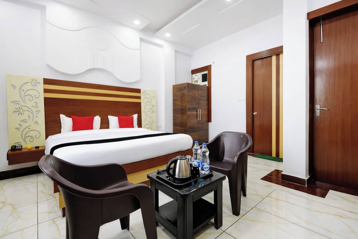 Habitación de hotel con cama, una mesita con hervidor y botellas, dos sillas, un armario y una puerta.