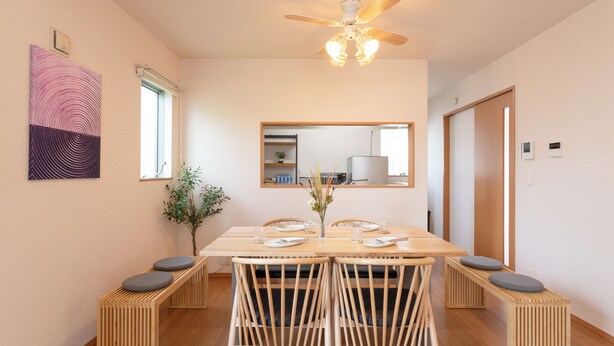 Un espace repas comprenant une table en bois, des chaises et des bancs, un ventilateur de plafond et un miroir au mur.