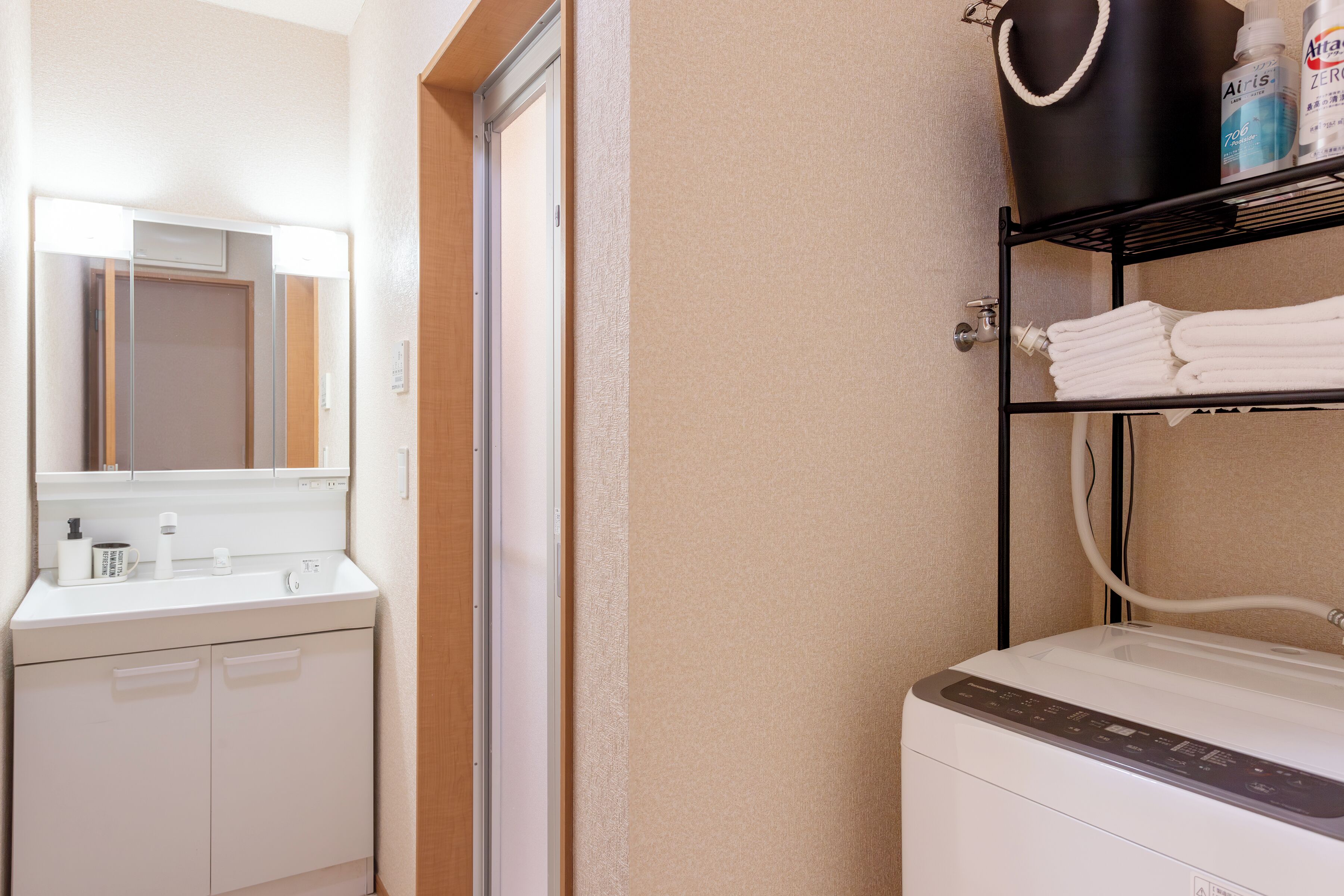Ein Badezimmer mit einem weißen Waschbecken, einem Spiegel, einem Handtuchhalter mit gefalteten Handtüchern und einem schwarzen Ablageschrank mit Toilettenartikeln.