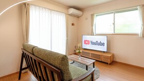 Un salon avec un canapé, une table basse en bois, un téléviseur affichant le logo de YouTube et une fenêtre avec des rideaux.