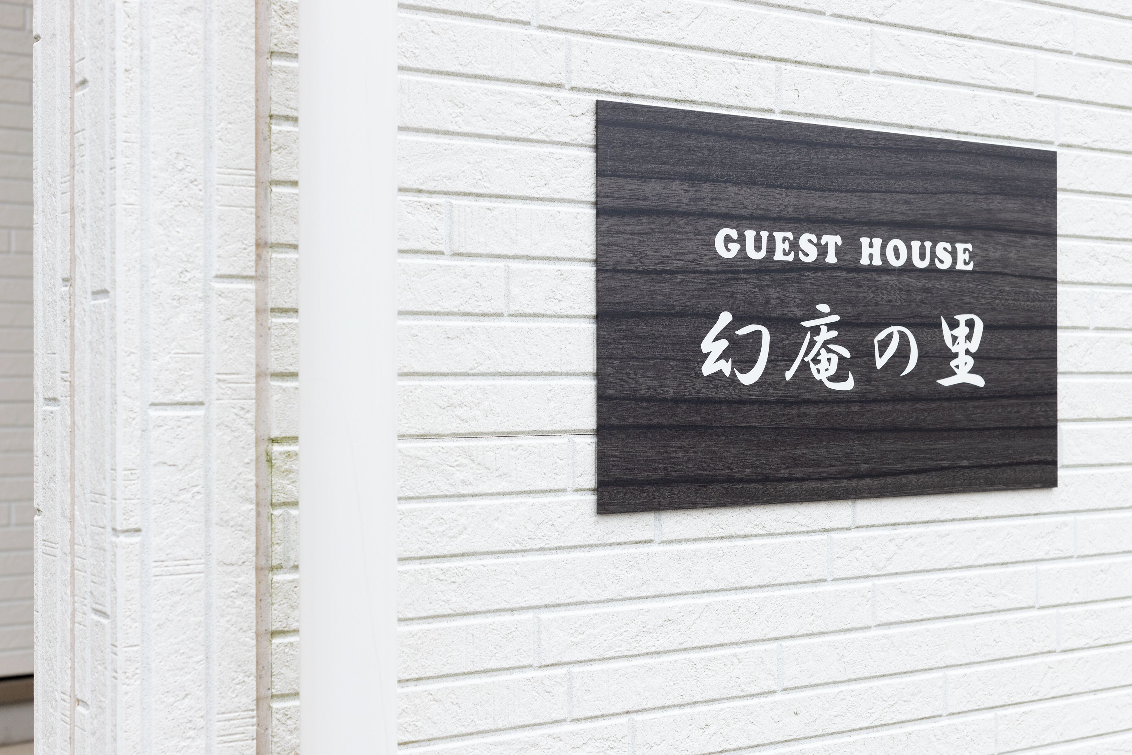 A sign on a white brick wall that reads 'GUEST HOUSE' with Japanese characters below.