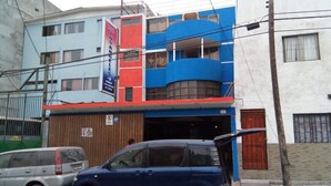 Ein mehrstöckiges Gebäude mit blau-roter Fassade, einem sichtbaren Garageneingang und einem geparkten Auto davor.