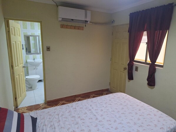 A bedroom with a bed, a window with curtains, a door, and an air conditioning unit.