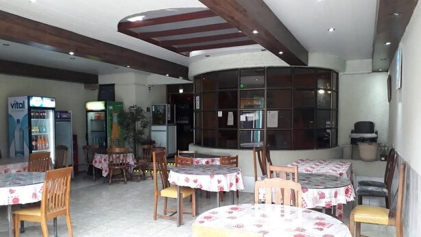Ein Restaurant mit runden Tischen, gedeckten mit floralen Tischdecken, hölzernen Stühlen und einer hohen Decke mit freiliegenden Balken.