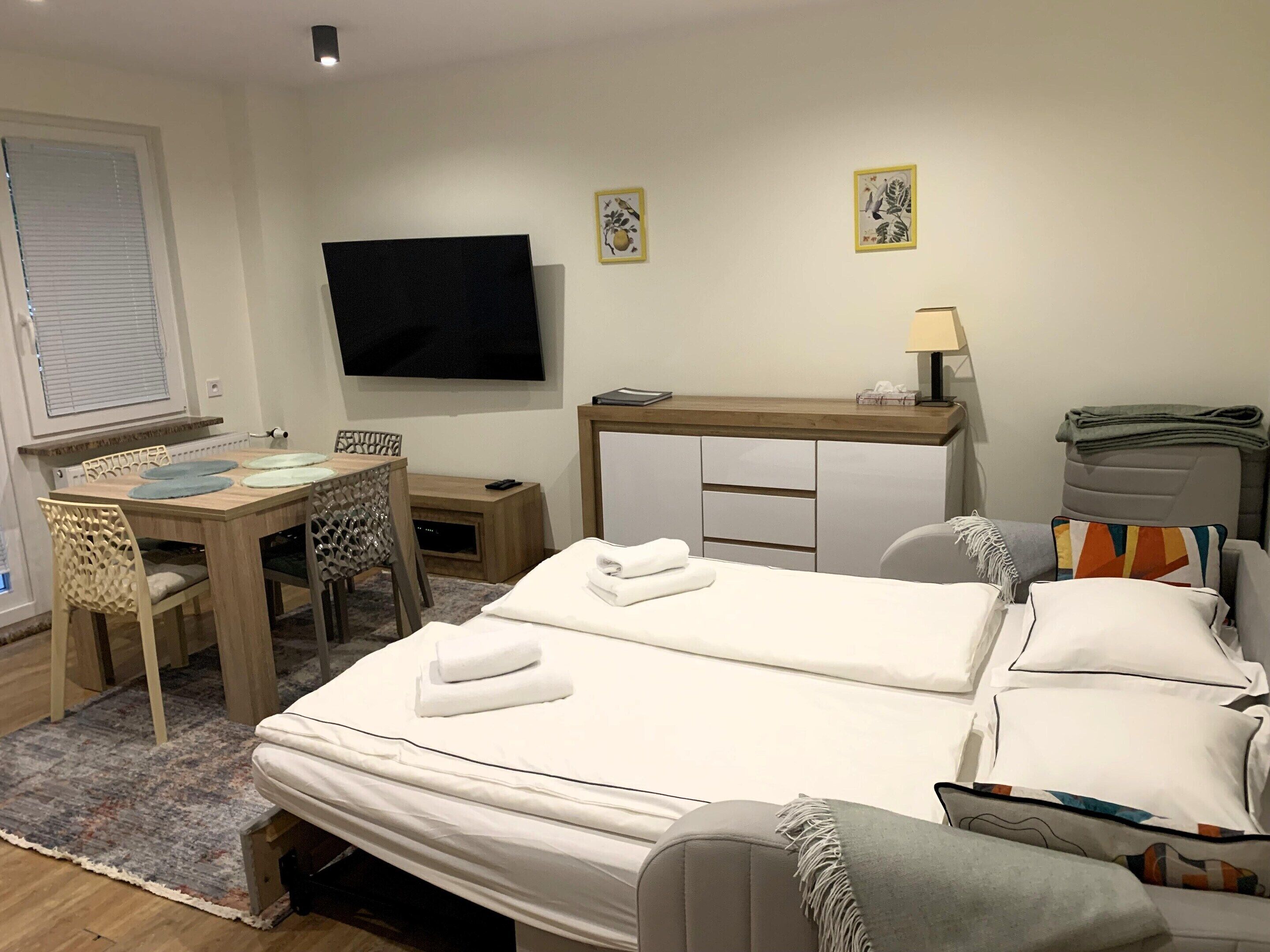 A hotel room with a bed, a desk with a chair, a television, and a small table with a lamp.