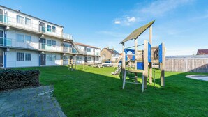 Ein Spielplatz mit Rutsche und Klettergerüst in einer grünen Umgebung, im Hintergrund Wohnhäuser.