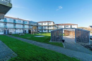 A courtyard with a playground, a wooden fence, and a building with multiple balconies. - Apartment by Dutch Dunes With Sea Views (Callantsoog)