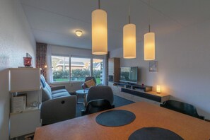A modern hotel room with a dining area, a sofa, a television, and a large window offering a view of the outdoors. - Apartment by Dutch Dunes With Sea Views (Callantsoog)