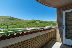A balcony with a view of a road and hills, a brick wall, and a door. - Apartment by Dutch Dunes With Sea Views (Callantsoog)