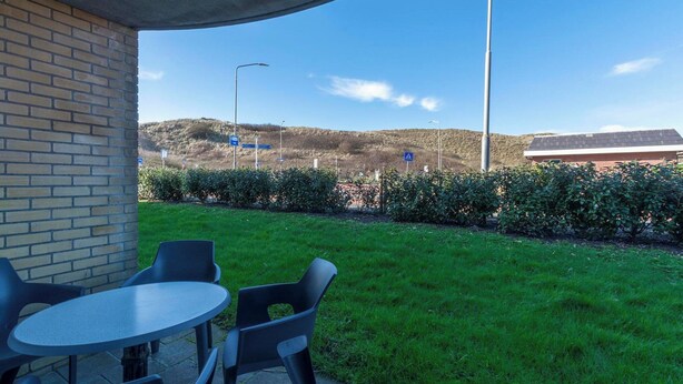 Eine Terrassenfläche mit Tisch und Stühlen, eine Ziegelmauer und Blick auf eine hügelige Landschaft.