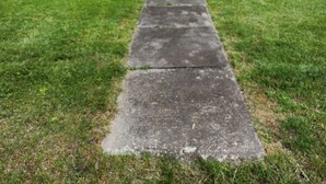 Una casa de dos pisos con base de piedra, un porche delantero y una bandera en la entrada.