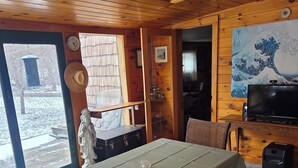Interior de madera con una mesa de comedor, sillas, un banco, un televisor y vistas a través de un ventanal.