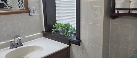 Une salle de bain avec un lavabo, un miroir, une fenêtre et des toilettes.