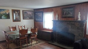 Un comedor con sillas de madera y una mesa, una chimenea de piedra y obras de arte enmarcadas en las paredes.
