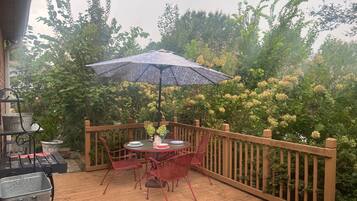 Une terrasse en bois avec une table et des chaises, entourée d’une clôture en bois et d’une végétation luxuriante.