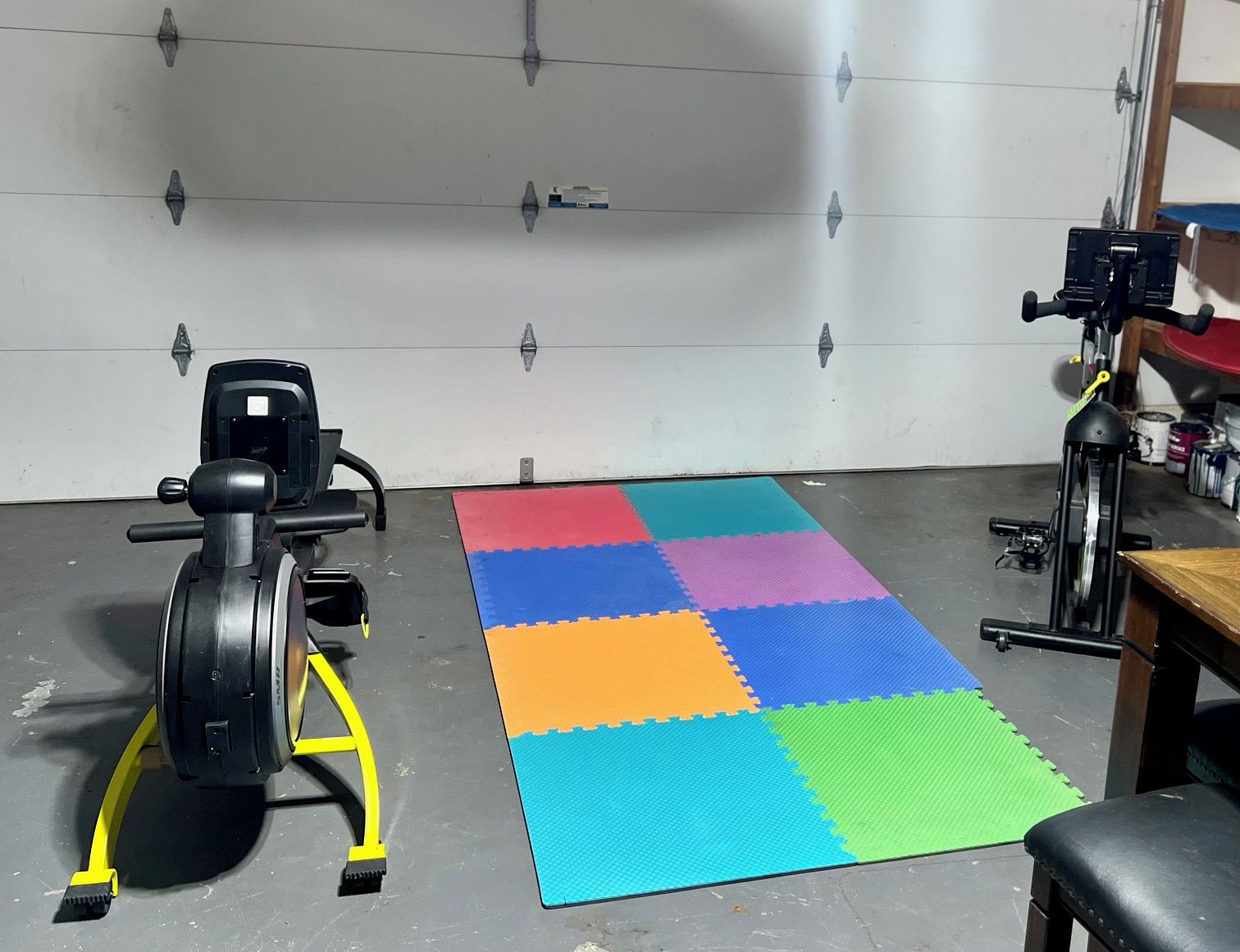 A room with a stationary bike, a treadmill, and a colorful mat on the floor.