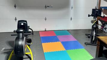 A room with a stationary bike, a treadmill, and a colorful mat on the floor.