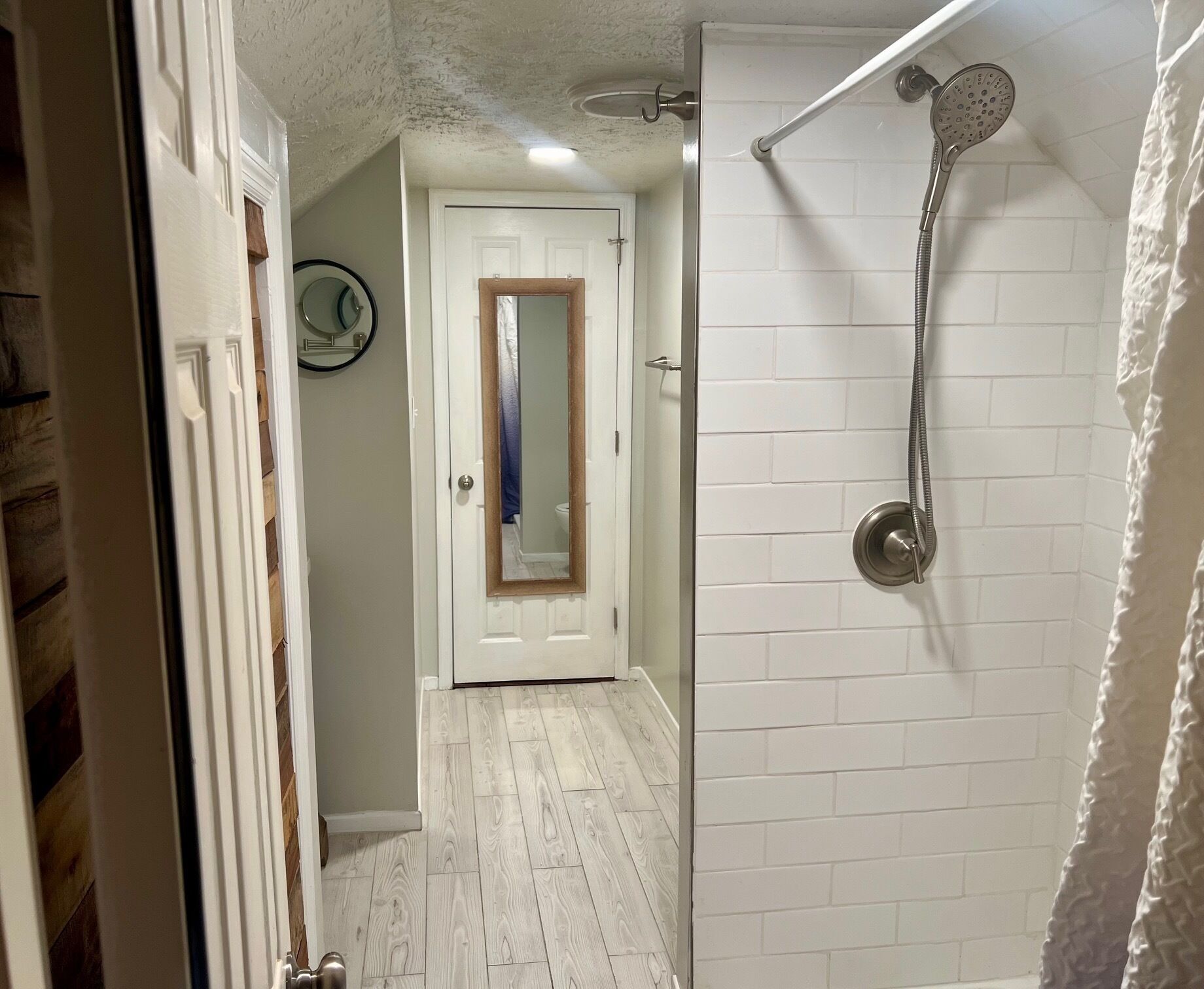 A bathroom with a shower, a mirror, and a door leading to another room.
