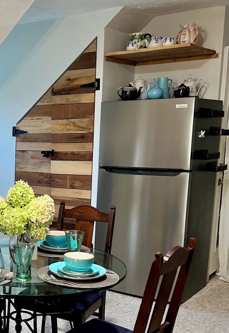 A kitchen with a stainless steel refrigerator, wooden wall paneling, and a dining table set with blue dishes.