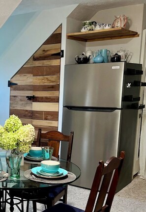 A kitchen with a stainless steel refrigerator, wooden wall paneling, and a dining table set with blue dishes. - Clarksville's Château Retreat (Clarksville)