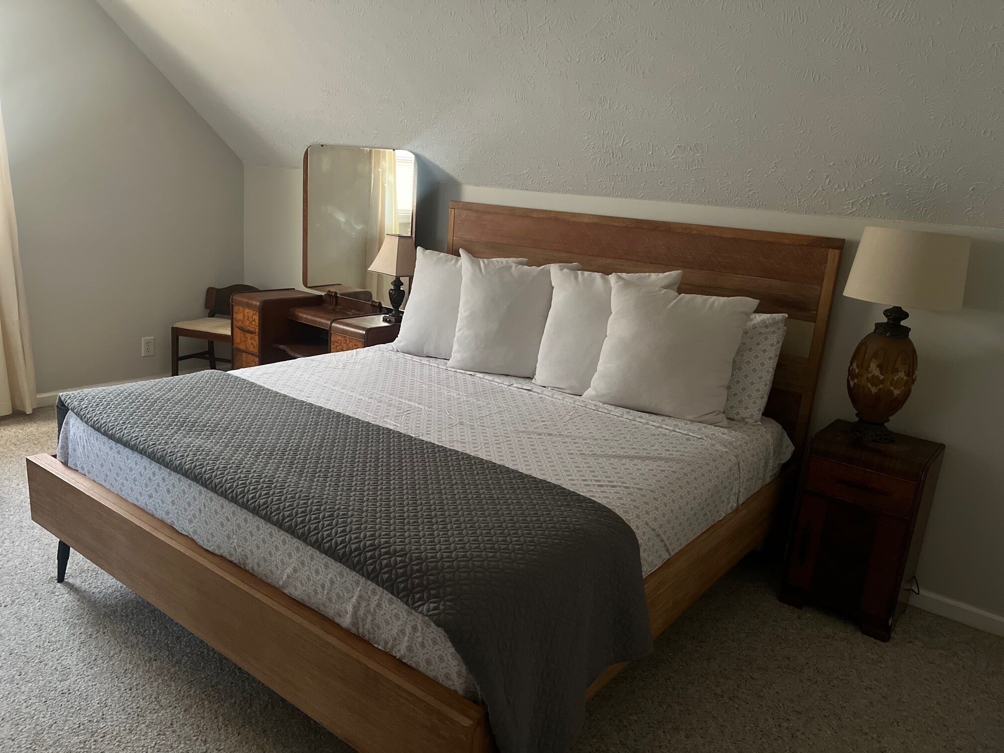A bedroom with a wooden bed, a nightstand with a lamp, a dresser, and a mirror.