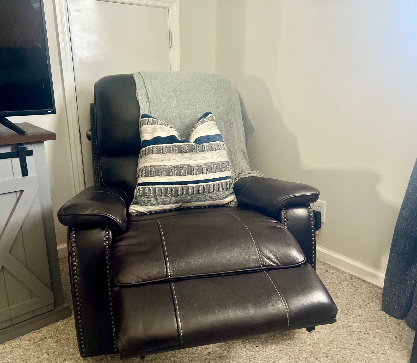 Un fauteuil inclinable en cuir noir avec un coussin décoratif à motifs.