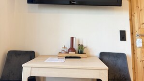 Una habitación con un televisor de pared, una mesa de madera, dos sillas, un florero y una planta pequeña.