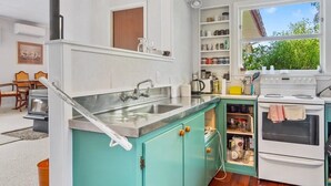 Una cocina con armarios color turquesa, una estufa blanca y una ventana con vistas a la vegetación.
