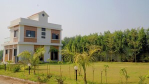 A modern two-story building with a flat roof, surrounded by a grassy area with small palm trees. - Mahi river villas Beautyful riverside location pet friendly fully furnished vill (Bamangam)