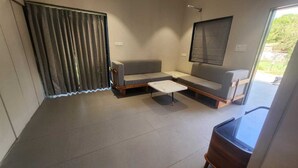 A room with a sofa, a small table, a window, and a curtain. - Mahi river villas Beautyful riverside location pet friendly fully furnished vill (Bamangam)
