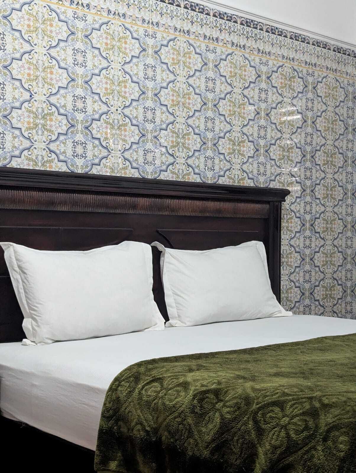 Una cama con ropa de cama blanca y dos almohadas, un cabecero de madera oscura y una manta verde estampada.