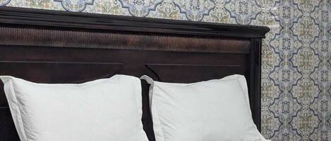 Una cama con ropa de cama blanca y dos almohadas, un cabecero de madera oscura y una manta verde estampada.