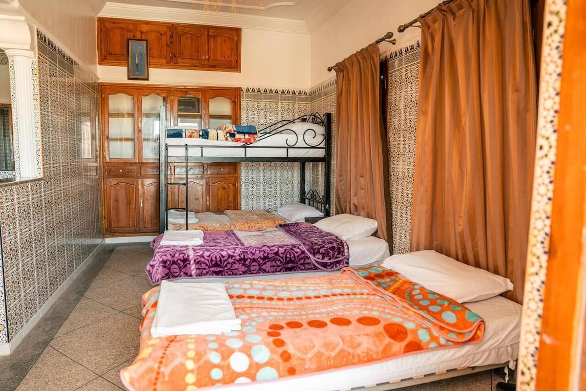A room with two beds, a kitchen area, and patterned walls.