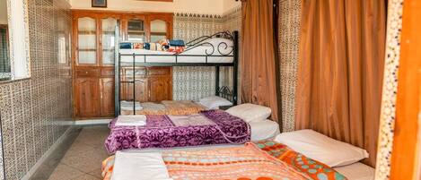 A room with two beds, a kitchen area, and patterned walls.
