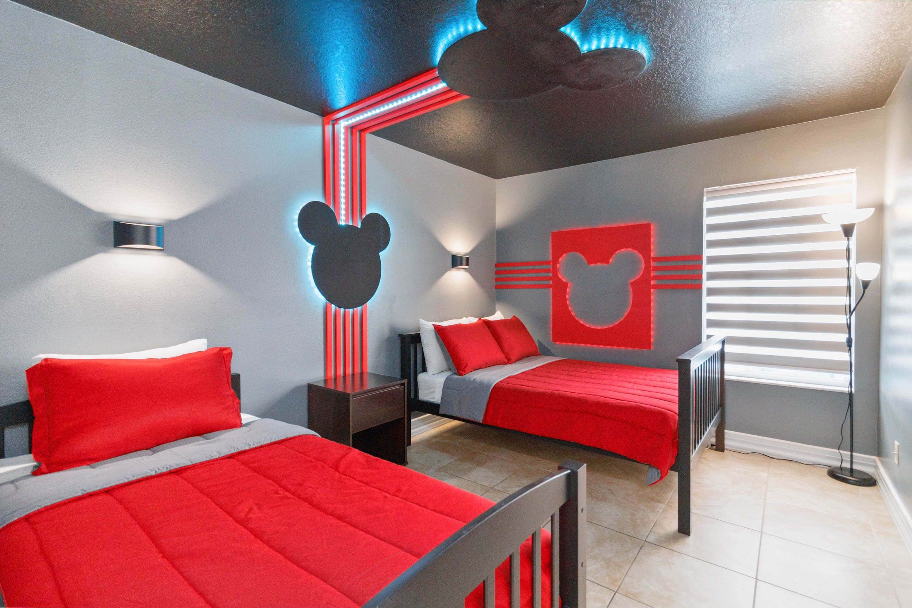 A bedroom with two beds, red bedding, and Mickey Mouse wall decorations.